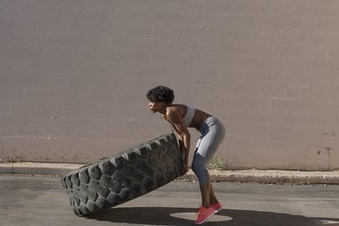 Woman lifting tire truck while exercising against wall