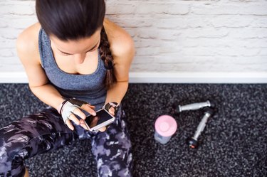 Fit woman in gym holding smartphone, brick wall