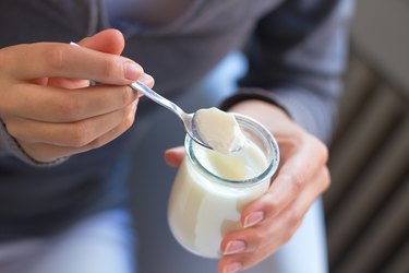 Close up of hands spooning white yogurt out of glass container as one of the best foods to lower blood pressure