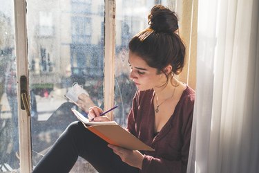 a young adult sits in a window writing in their diary as a free way to improve wellbeing