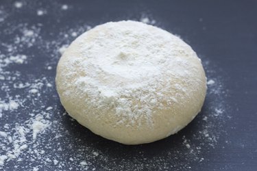 fresh raw baking dough sprinkled with flour on a dark background