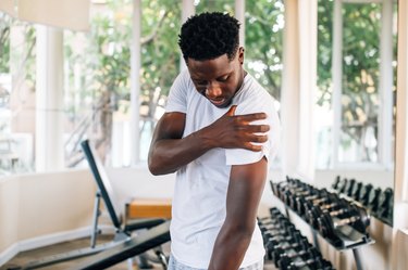 Sportsman holding shoulder that pops and cracks in gym