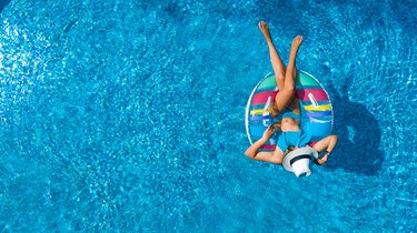Aerial view of person in swimming pool from above, swim on inflatable ring donut and has fun in water on family vacation