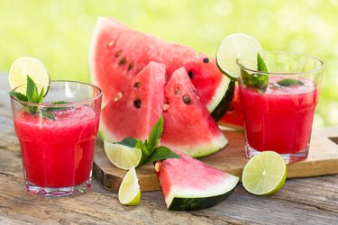 two glasses of watermelon smoothies with lime and mint next to slices of watermelon on a wooden cutting board