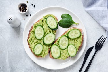 Toasts with avocado and cucumber on white plate