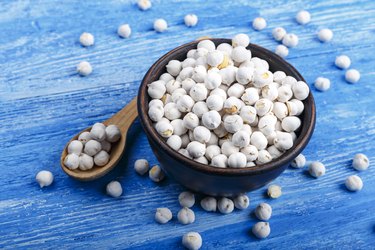 Dry chickpeas in a clay plate with a spoon on a blue wooden background.