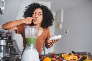 Woman tasting green smoothie from a blender in the kitchen
