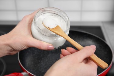 Woman putting coconut oil into frying pan