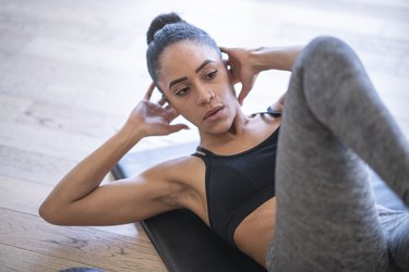 Close up of person wearing gray leggings and black top doing crunches to target belly fat at home.