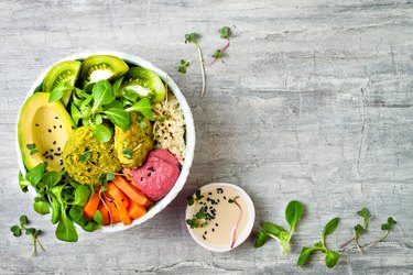Middle eastern style Buddha bowl with green falafel, quinoa, butternut squash, tomatoes, avocado, beetroot hummus, micro greens and tahini sauce.