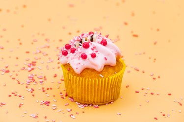 Decorating a Cupcake with Sprinkles on orange pastel background.