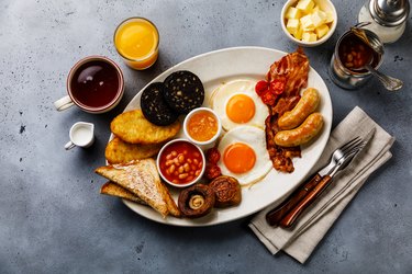 Full fry up English breakfast with fried eggs, sausages, bacon, black pudding, beans, toasts and tea