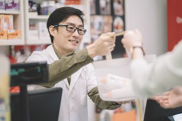 一个亚洲的中国男性药剂师接管他的顾客的购物篮和微笑在药房商店