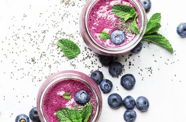 Purple homemade smoothie with blueberries, chia seeds and mint leaves in glass jars on white background, flat lay, top view