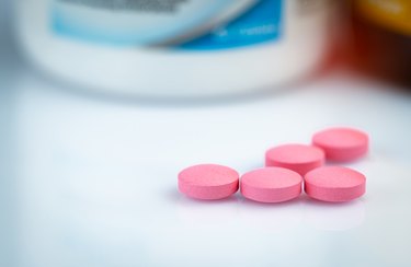 Round pink tablets pill on blurred drug bottle. Vitamins and minerals plus folic acid vitamin E and zinc in drug bottle on gradient background. Pink tablets pills fr during and after pregnancy woman.