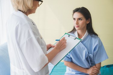 Senior woman doctor and patient discussing and making notes about symptom problem while she sitting on the bed.