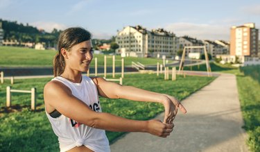 Woman looking away while stretching wrist at park