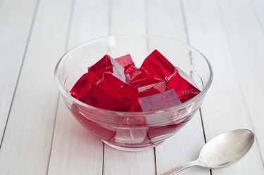 Red jelly cubes in glass bowl with silver spoon