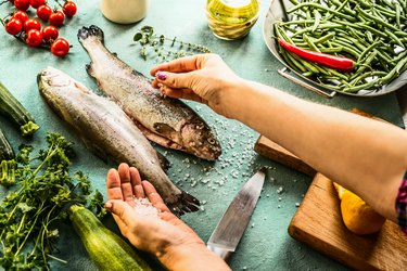 Female woman hands sprinkle with salt raw trout fishes for keto electrolytes