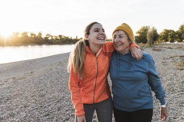 Fit grandmother and granddaughter walking at the river with arms around, having fun