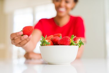 Woman eating fresh red strawberries at home on weight-loss journey