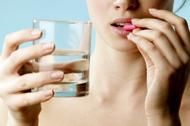 a close up photo of a person taking a pink vitamin and holding a glass of water