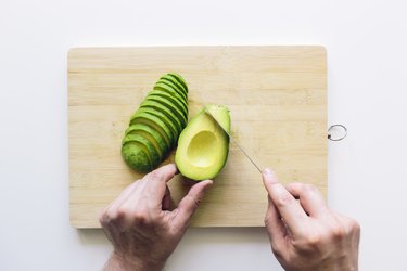 Person cutting avocado - a food for healthy hair - on a wooden cutting board, personal perspective directly above view
