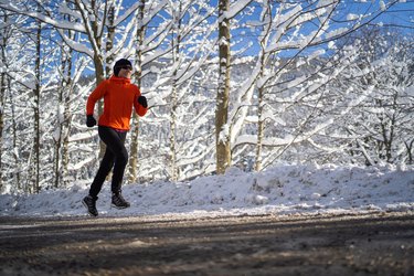 在阳光明媚的寒冷日子里，女人慢跑在雪地里的乡村风景