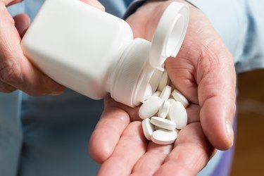 Woman hand holds white medication pills, pours from a white bottle into palm the magnesium tablets dietary supplement