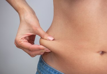 Girl pulls hand the skin on the abdomen, showing the body fat in the abdominal area and sides