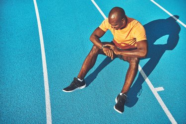 Young athlete sitting on a track checking his running time