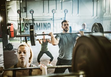 Group of athletic people having weight training with barbells in a health club listing to weight lifting music.