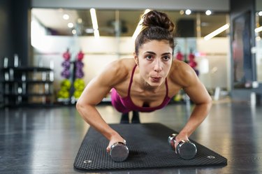 Woman doing push-ups exercise with dumbbell in a fitness workout