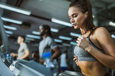 Determined female athlete jogging on treadmill in a gym.