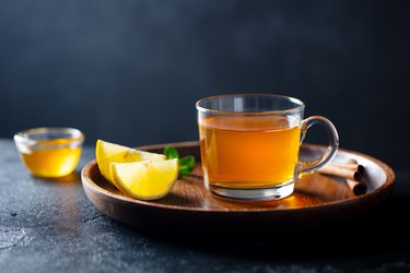 Tea cup with honey and lemon on wooden tray. Grey background. Copy space.