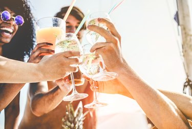 Group of happy friends cheering with tropical cocktails at boat party - Young people having fun in caribbean sea tour - Youth and summer vacation concept - Focus on bottom hands glass