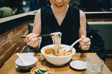 Asian woman eating soup noodles joyfully in restaurant