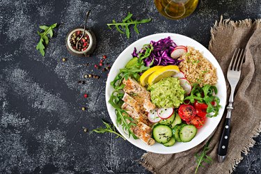 Healthy dinner. Buddha bowl lunch with grilled chicken and quinoa, tomato, guacamole, red cabbage, cucumber and arugula on gray background. Flat lay. Top view