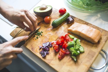 Woman preparing vegetables and salmon on chopping board for Mediterranean diet