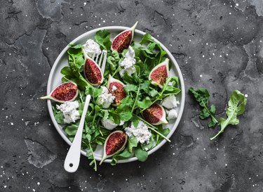 Figs, goat cheese, arugula salad on dark background, top view