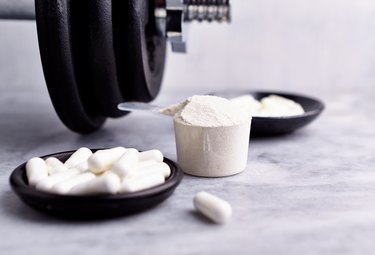 Creatine, Taurine capsules and a dumbbell. Bodybuilding food supplements on stone / wooden background. Close up. Copy space.