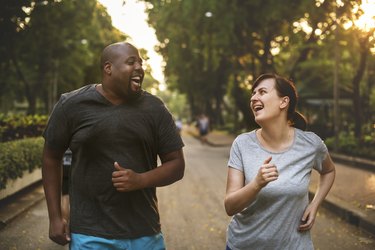 A smiling couple running together in the park to help prevent high blood pressure