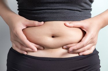 Midsection Of Woman Touching Stomach Against Gray Background