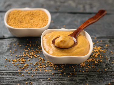 Two bowls and spoon with seeds and mustard sauce on a dark rustic table.