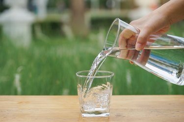 hand pouring water from glass bottle into glass on wooden table outside