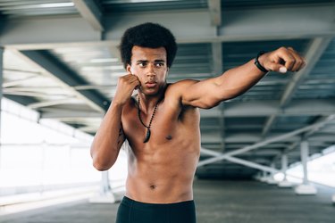 man practicing kickboxing under a bridge, throwing a punch in front