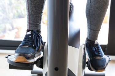 Unrecognizable Female Athlete Exercising on Stationary Bike at Home - Stock Photo