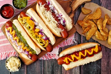 overhead photo of four hot dogs with toppings and a side of potato wedges on a wooden picnic table