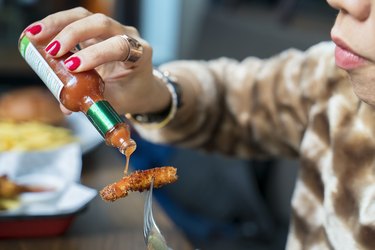 Woman adding hot sauces on crispy, crunchy fried chicken. Fast food