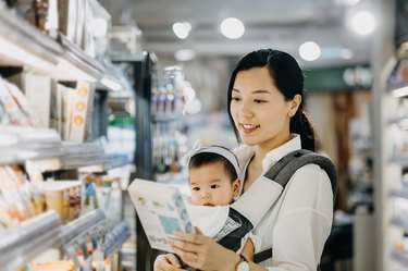 Beautiful Asian mother carrying cute baby girl shopping for organic baby food in grocery store